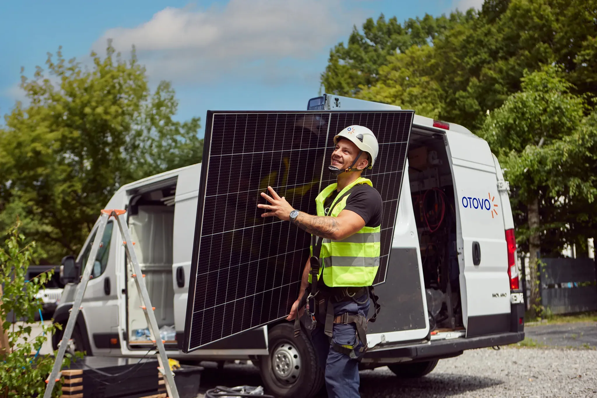 En smilende installatør bærer et solcellepanel ut fra en varebil