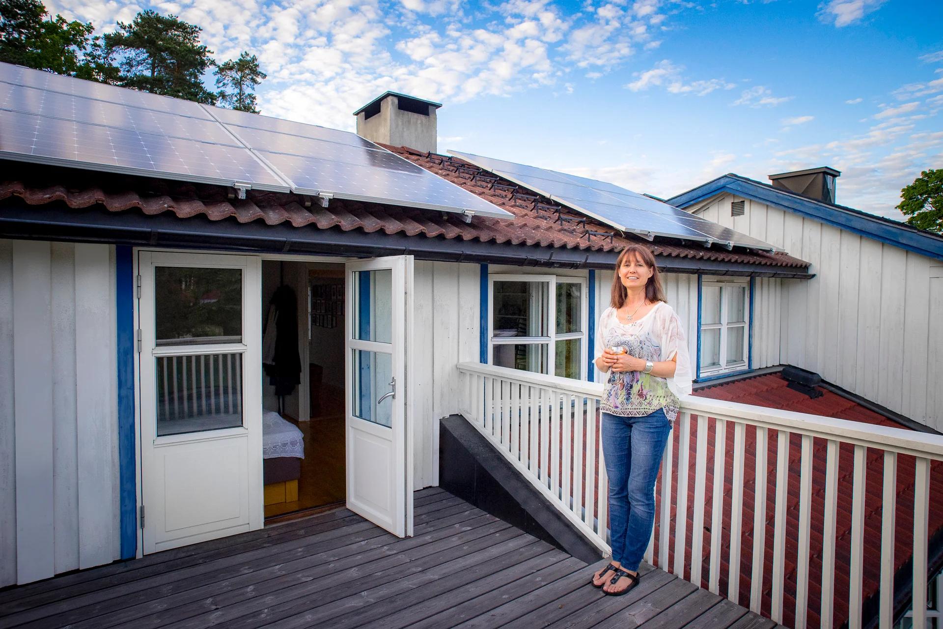 En kvinne står på terassen foran en skrå takflate med solcellepaneler på