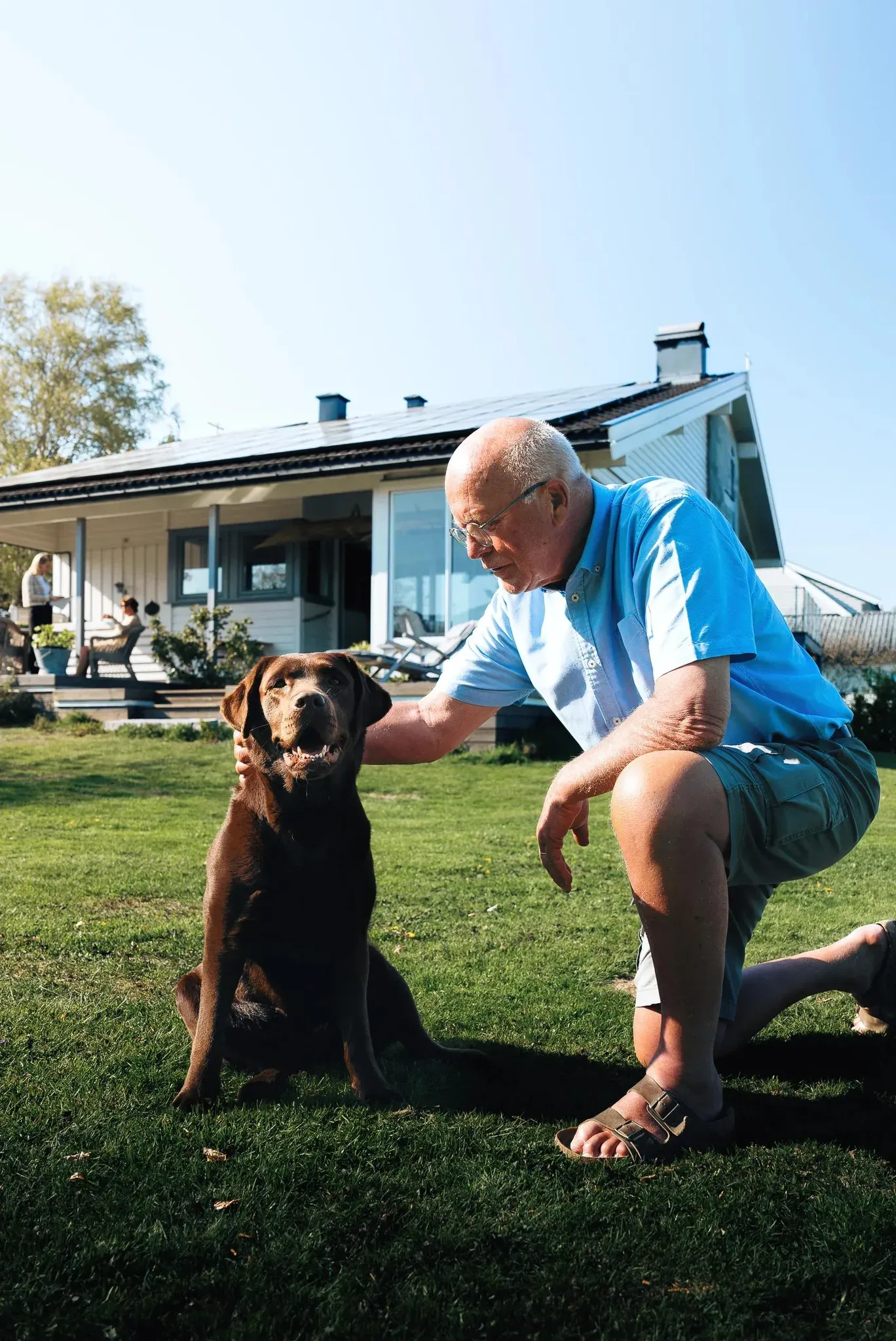 En man klapper en hund foran et hus med solcellepaneler på taket